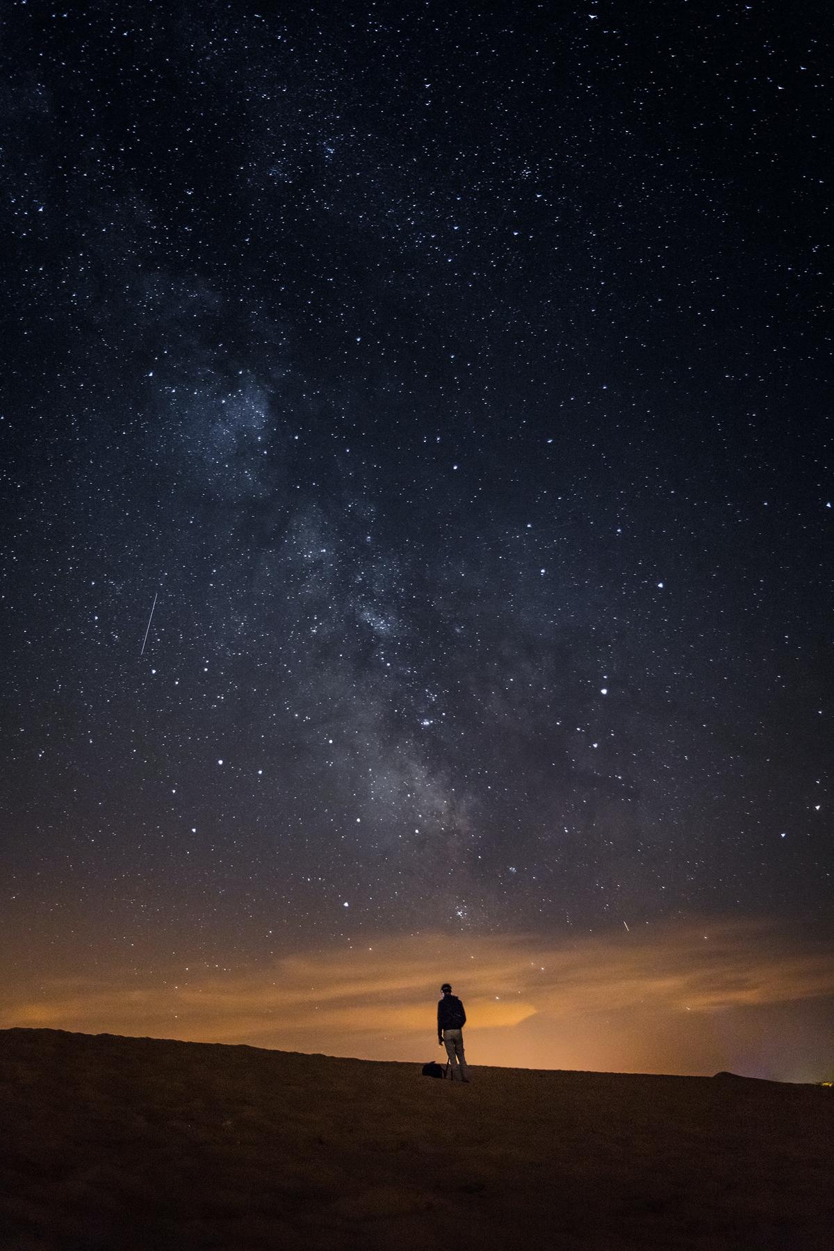 A person pointing a camera towards the night sky with stars and the Milky Way visible in the background.
