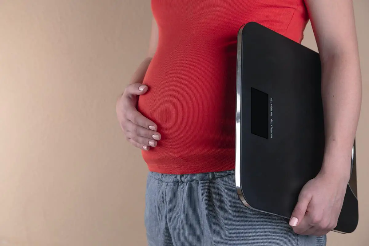 A photograph of a pregnant woman holding her belly with both hands. The image is taken with a camera that blurs the background slightly and focuses solely on the woman and her pregnancy bump. The image conveys a feeling of anticipation and wonder.
