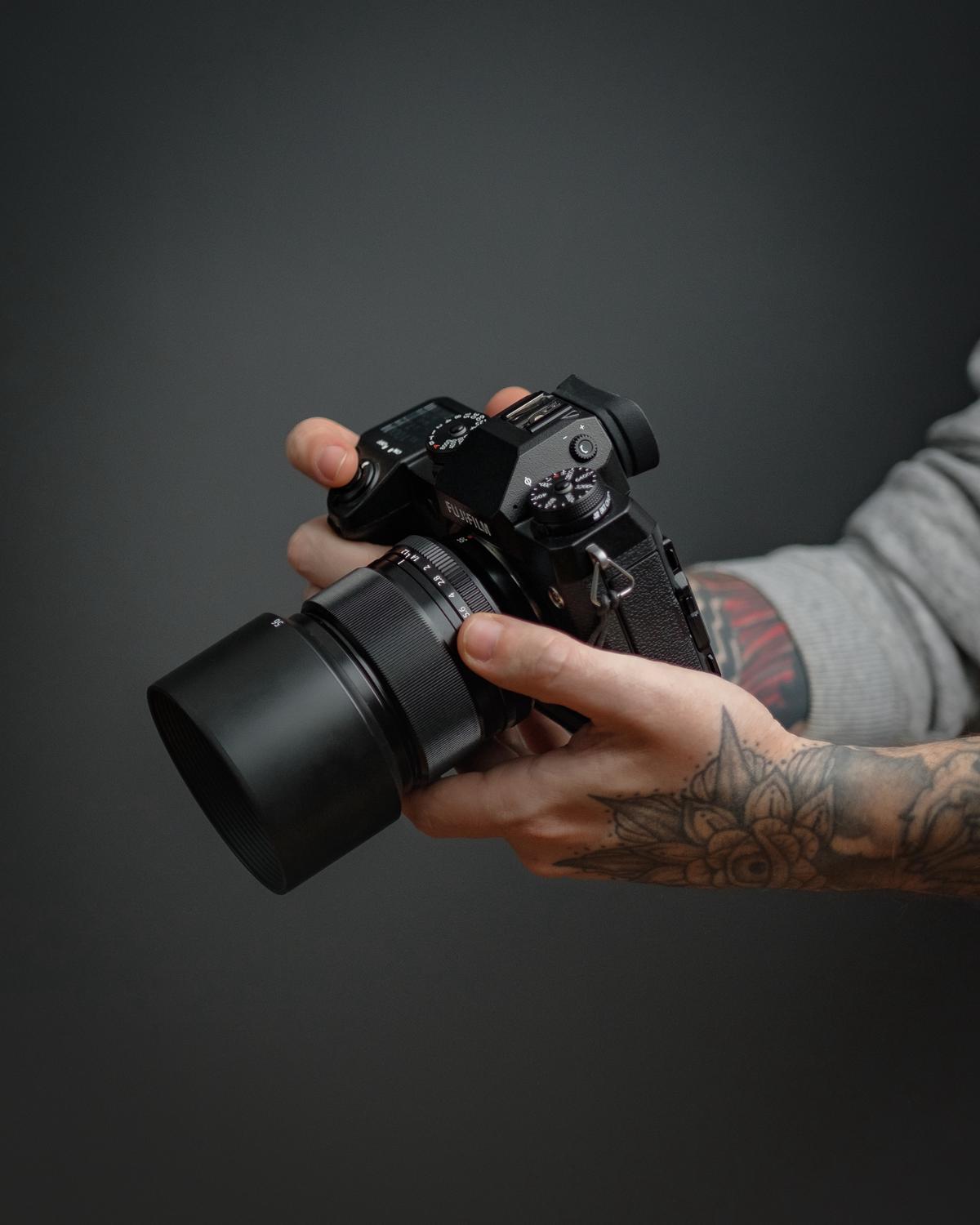 A DSLR camera and lenses, a mirrorless camera and lenses, and a point-and-shoot camera with the caption 'Popular Lens Choices for Travel Photography' written on a blurred background