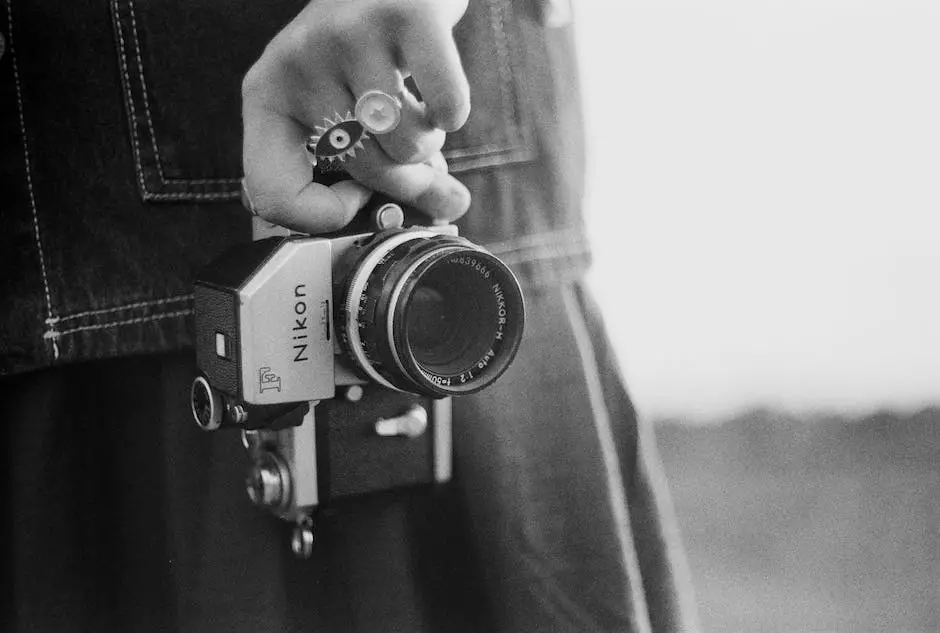 A black and white image of a hand holding a film camera with the Nikon logo visible on the front of the camera.
