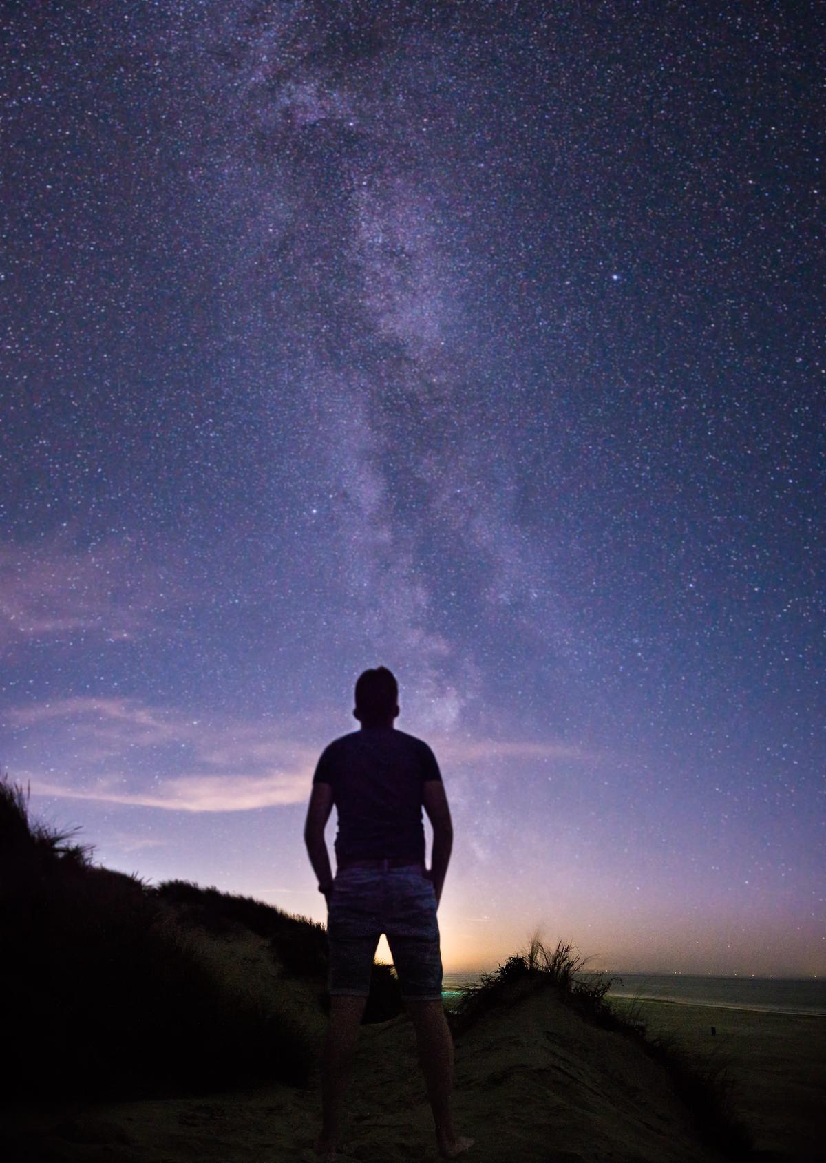 A person standing on a hill looking up at the night sky filled with stars.