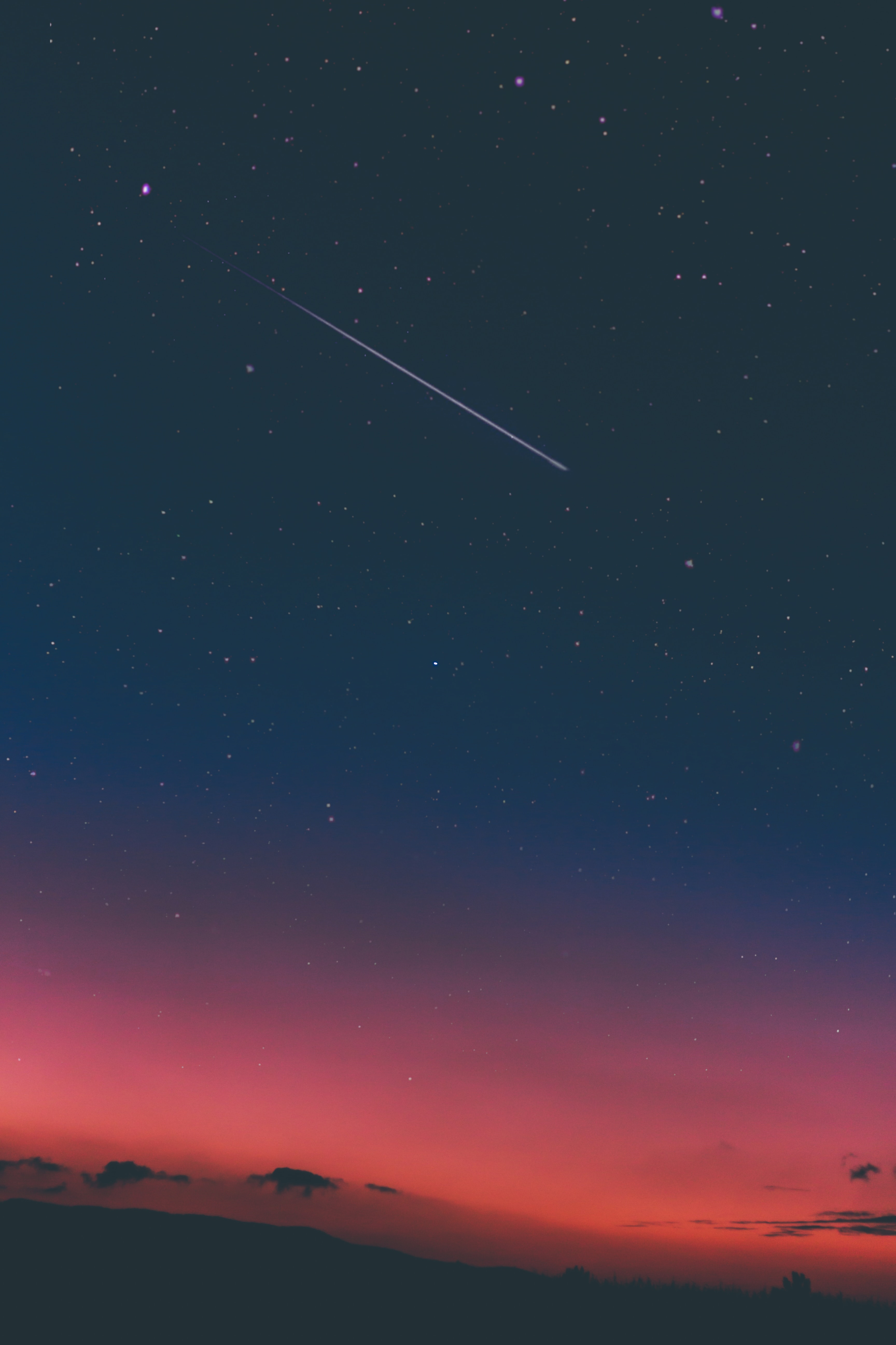 A photo of a dark sky filled with stars and a shooting star streaking through the middle of the photo.