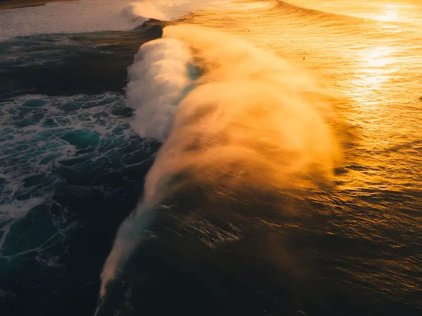A surf photographer captures a surfer riding a big wave with the sun setting over the ocean in the background.